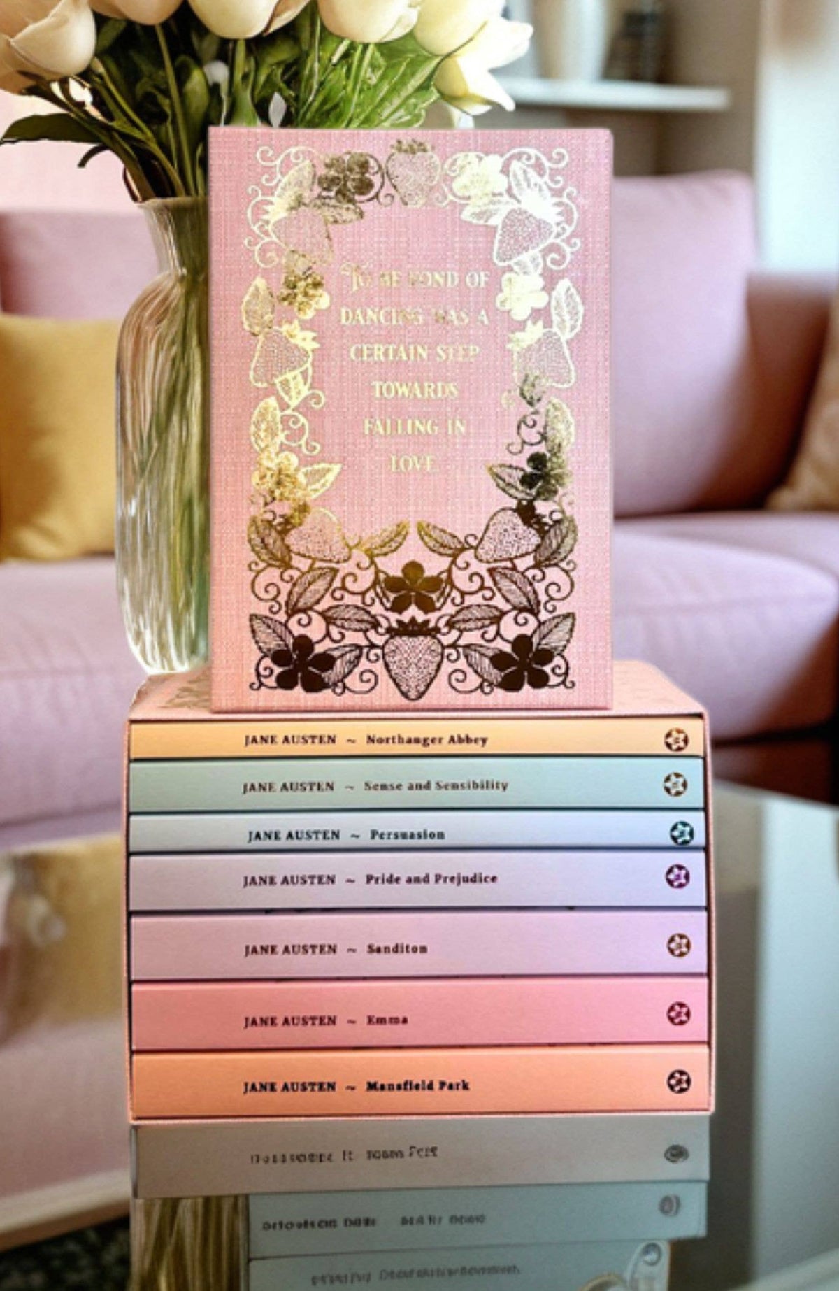 Stack of Jane Austen books with decorative cover and vase of flowers on a blurred background