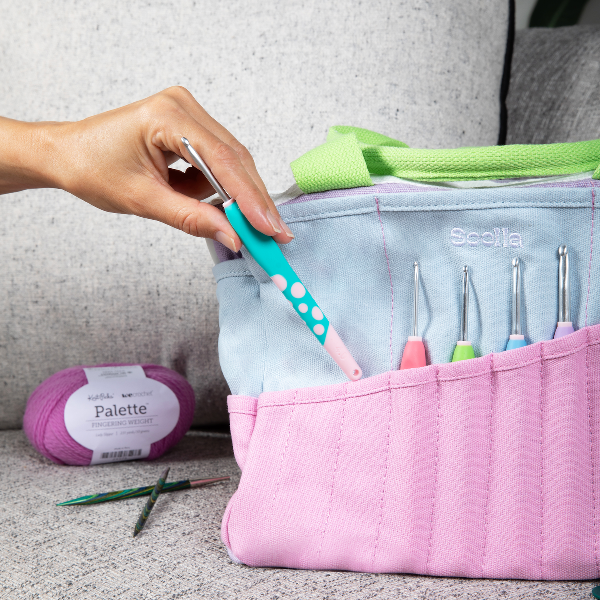 Pink Soolla Studio Artist Bag crochet hook case with various hooks, yarn, and a hand holding a teal and pink hook.