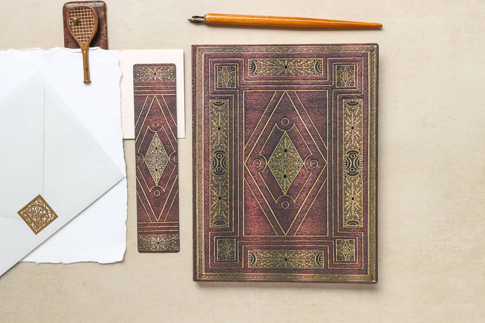 Decorative Shakespeare First Folio midi lined journal with ornate cover on a beige surface with a pen and envelope.