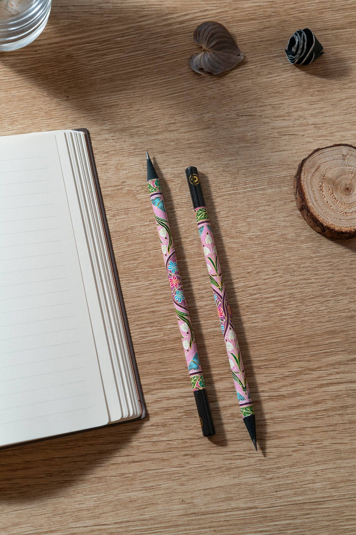 Two decorative pens on a wooden surface with an open notebook.
