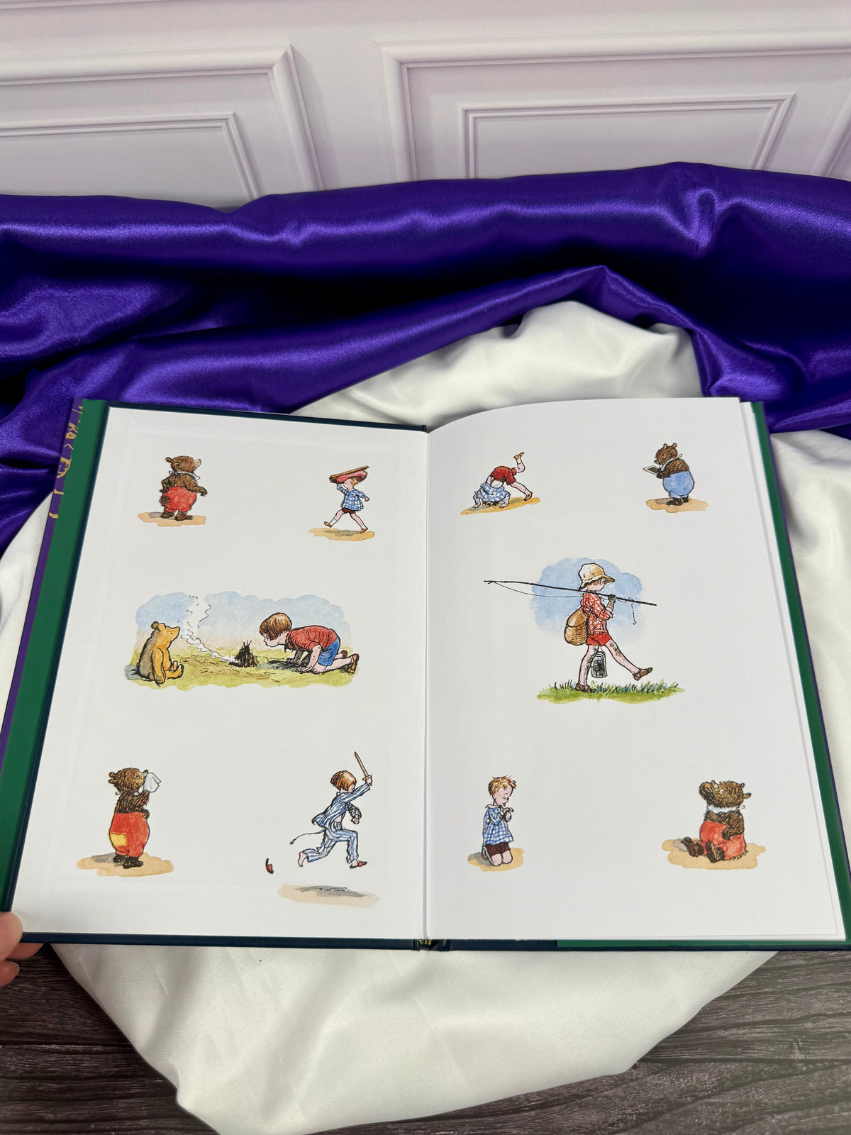 Now We Are Six hardcover opened to colorful E. H. Shepard illustrations of Christopher Robin and Winnie-the-Pooh playing, walking, and exploring.
