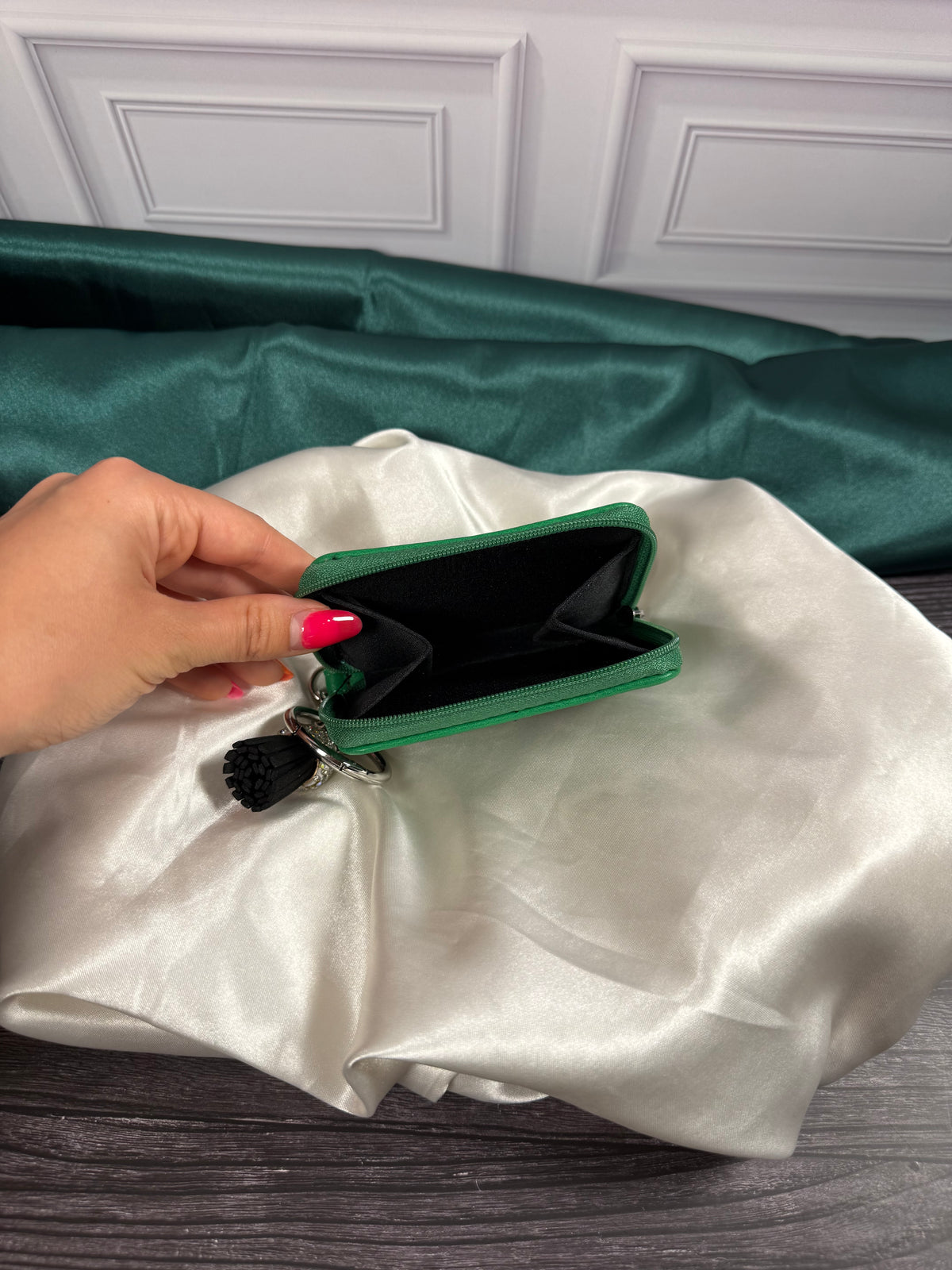The Wizard of Oz miniature book coin purse held open to show its black interior compartment and green zippered closure, displayed on ivory satin.