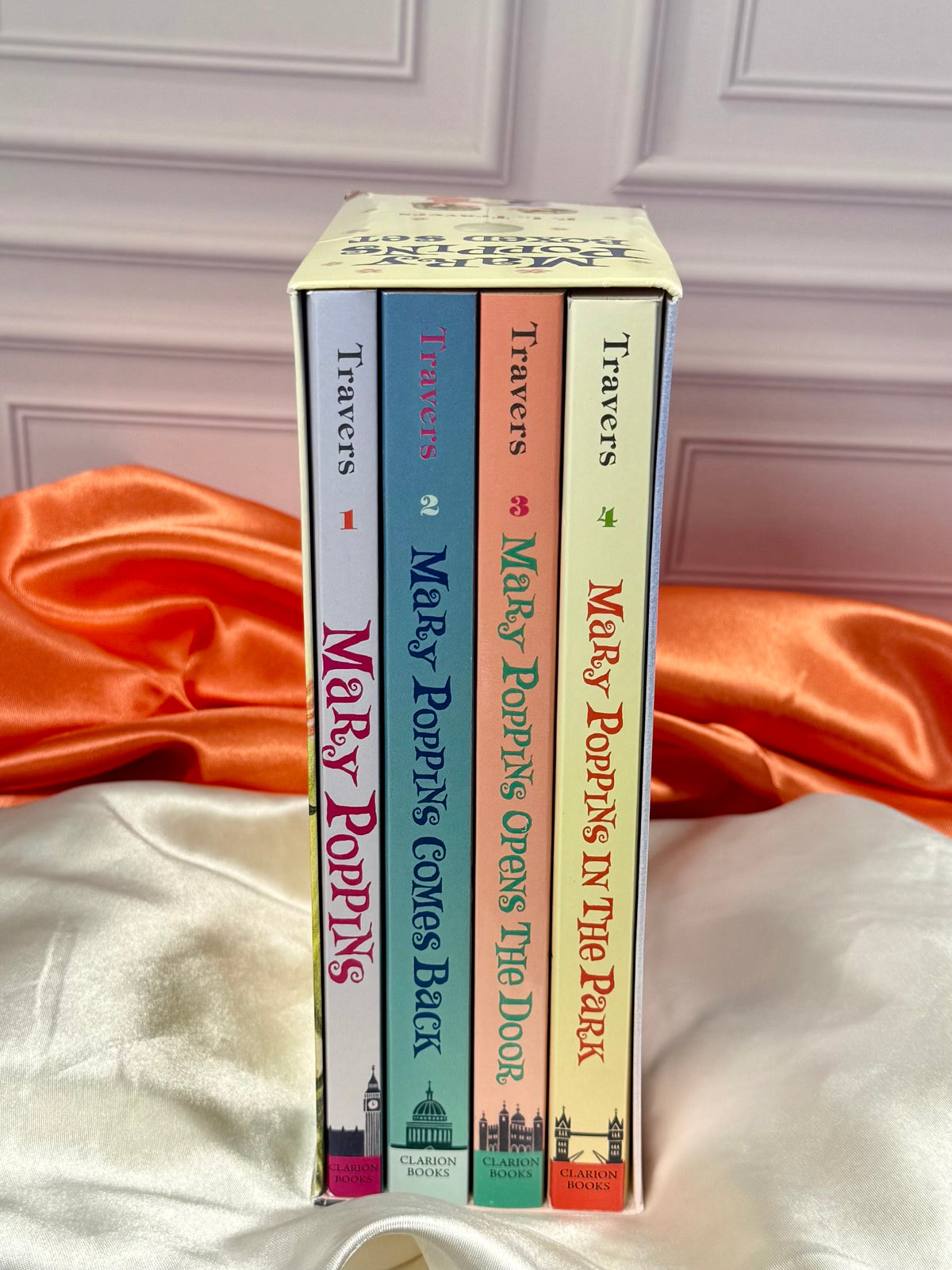 Side view of the Mary Poppins four-book paperback collection showing the colorful book spines displayed on ivory and red satin fabric.