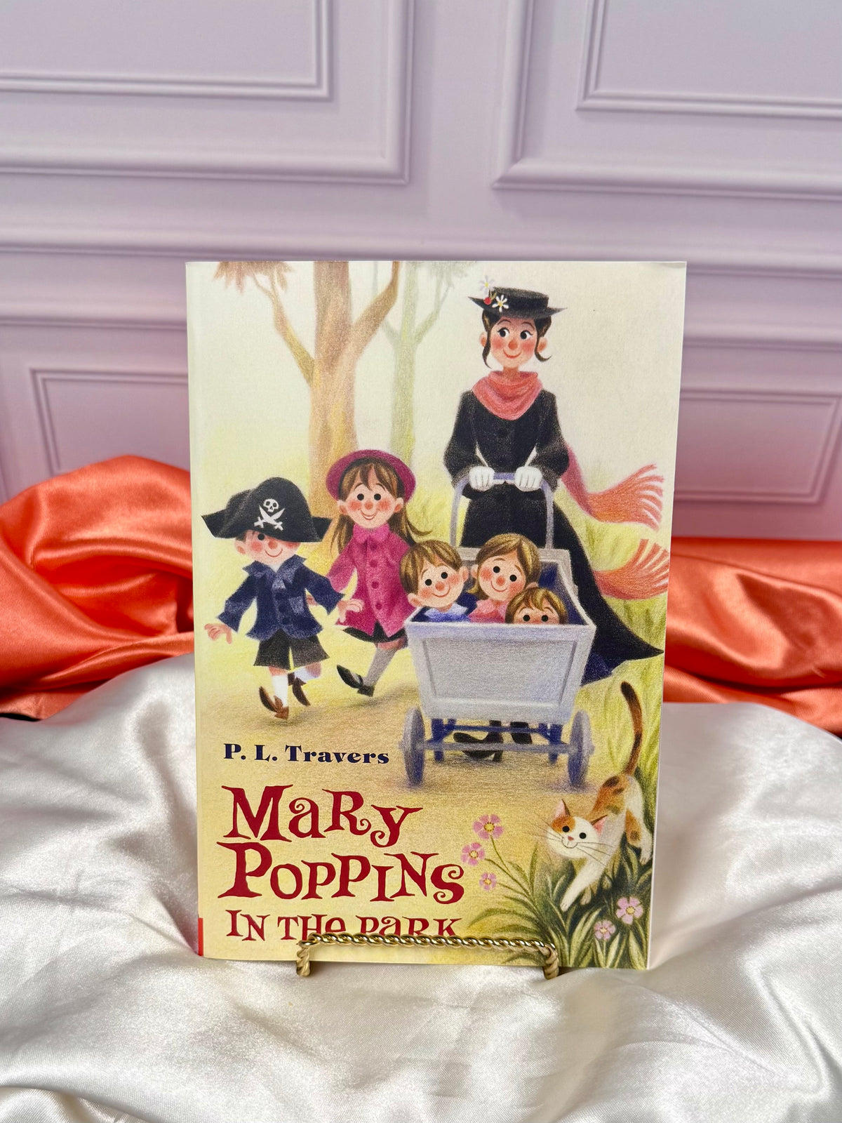 Illustrated Mary Poppins In the Parkpaperback from the four-book collection, displayed upright against a white paneled background with red satin fabric.