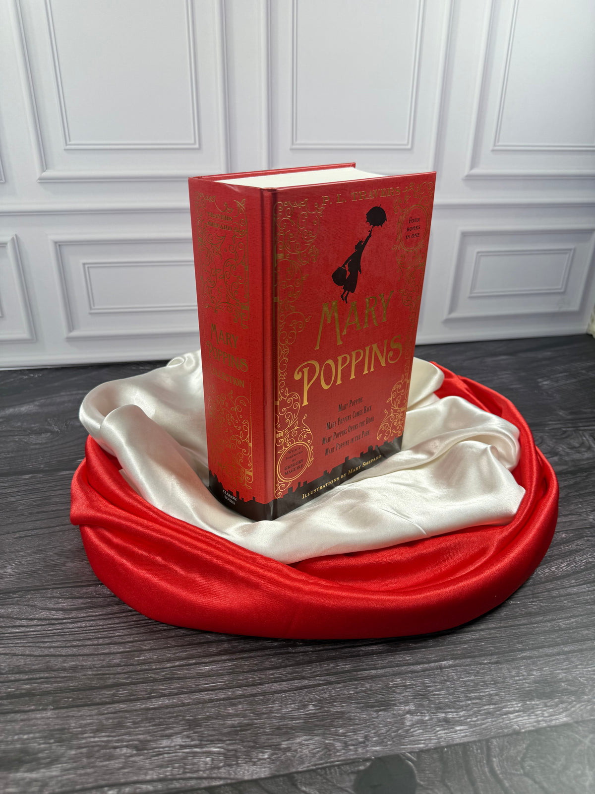 Angled view of the red Mary Poppins Collection hardcover treasury showing its decorative cover and thick binding on a satin-draped book stand.