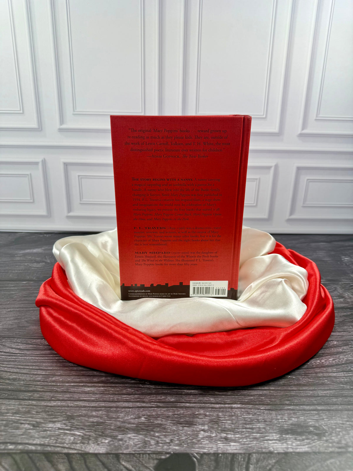 Rear view of the red Mary Poppins Collection hardcover treasury displayed on a black book stand with ivory and red satin fabric.