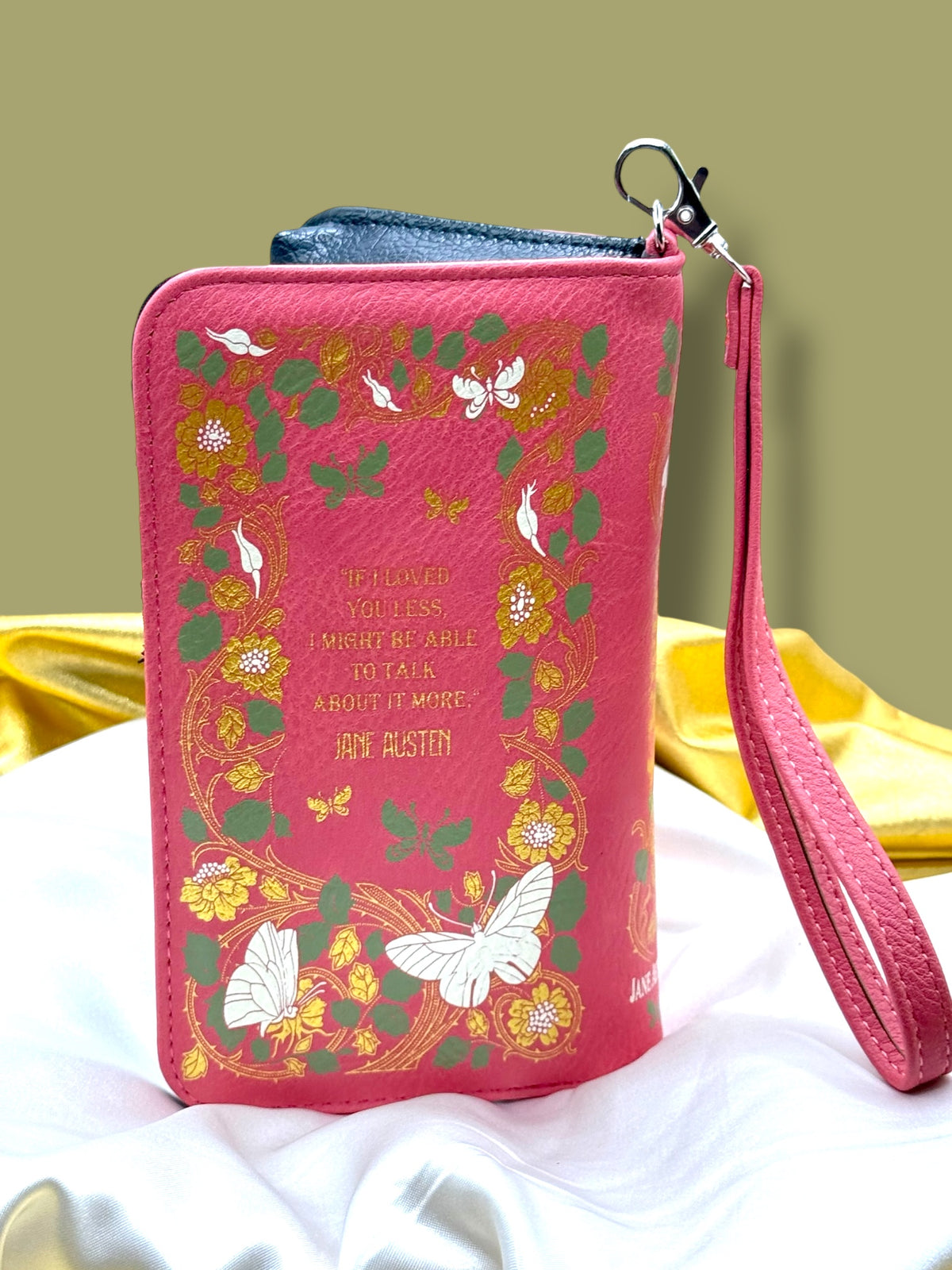 Emma Book Wallet photographed from the back, showing its book-shaped construction, decorative cover, and attached wristlet strap.