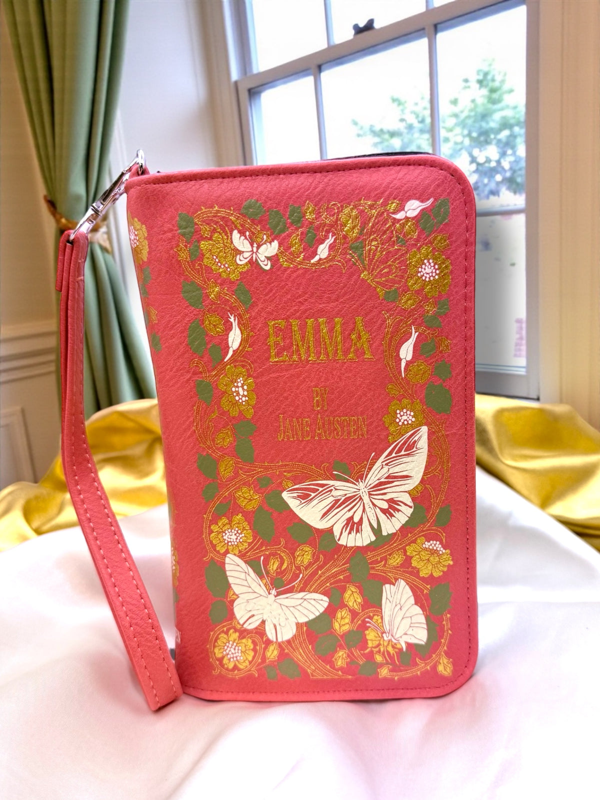 Emma by Jane Austen literary book wallet shown against a white background, featuring a pink floral cover design and matching wristlet strap.