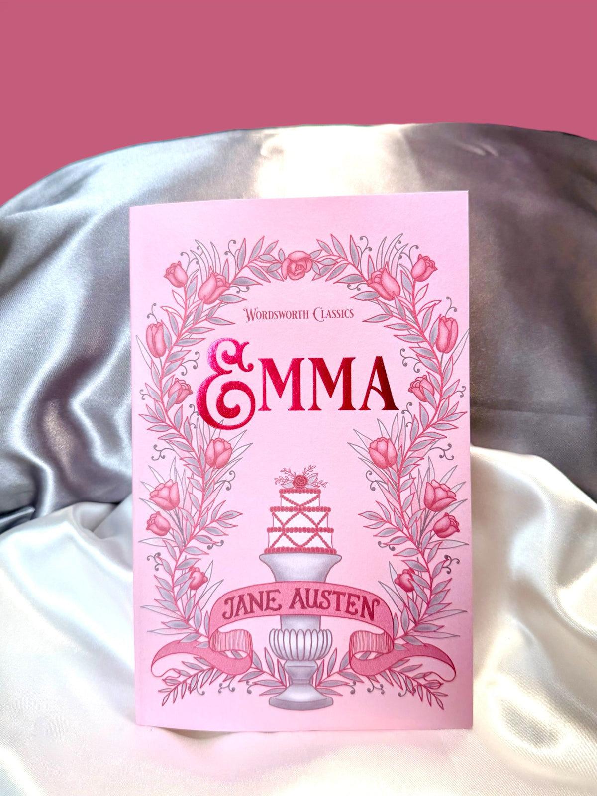 Emma by Jane Austen, Wordsworth Classics paperback with a decorative pink illustrated cover, photographed against soft satin fabric.