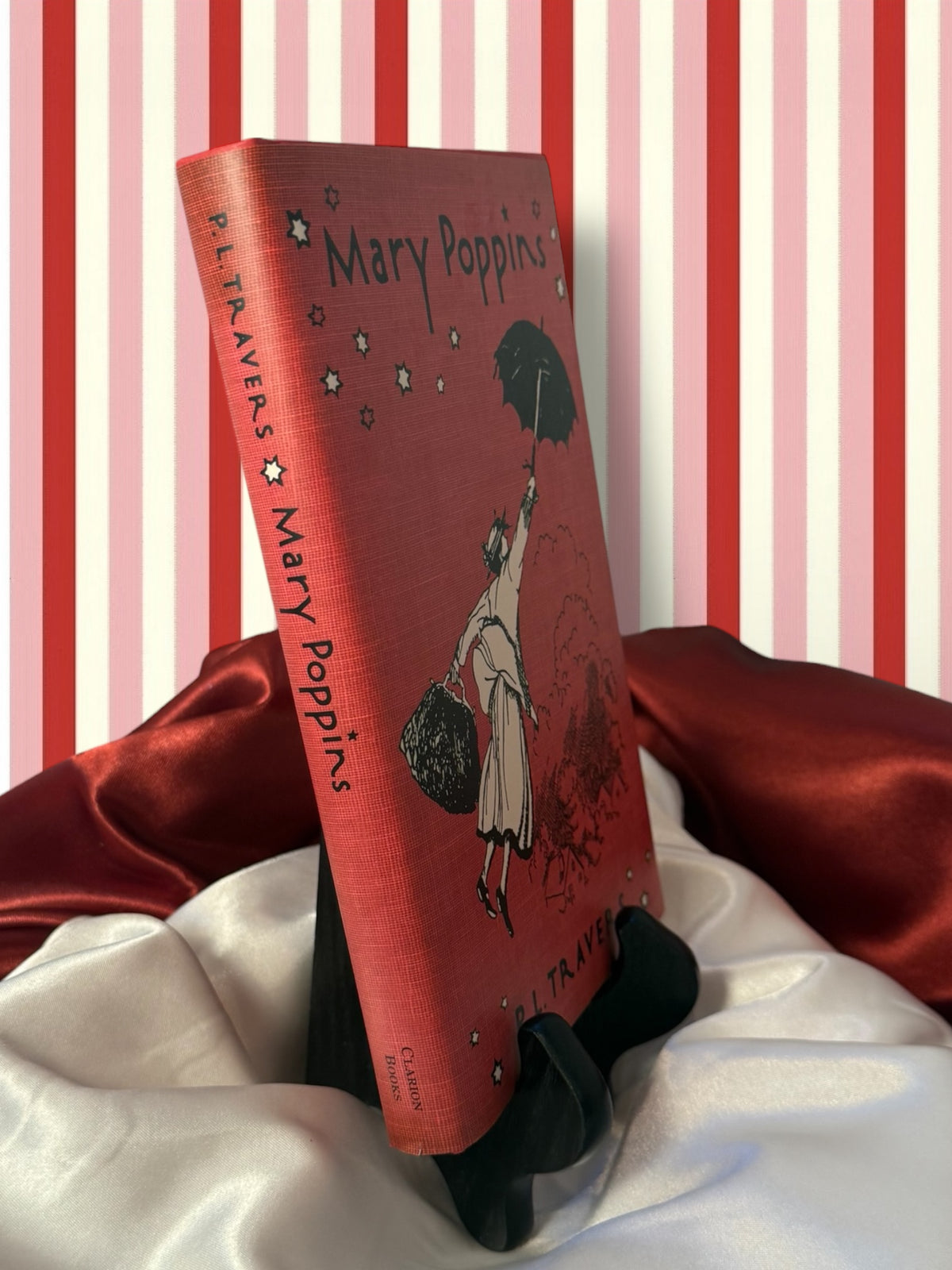 Angled view of the Mary Poppins hardcover by P. L. Travers, showing its red illustrated book jacket and spine on a decorative book stand.
