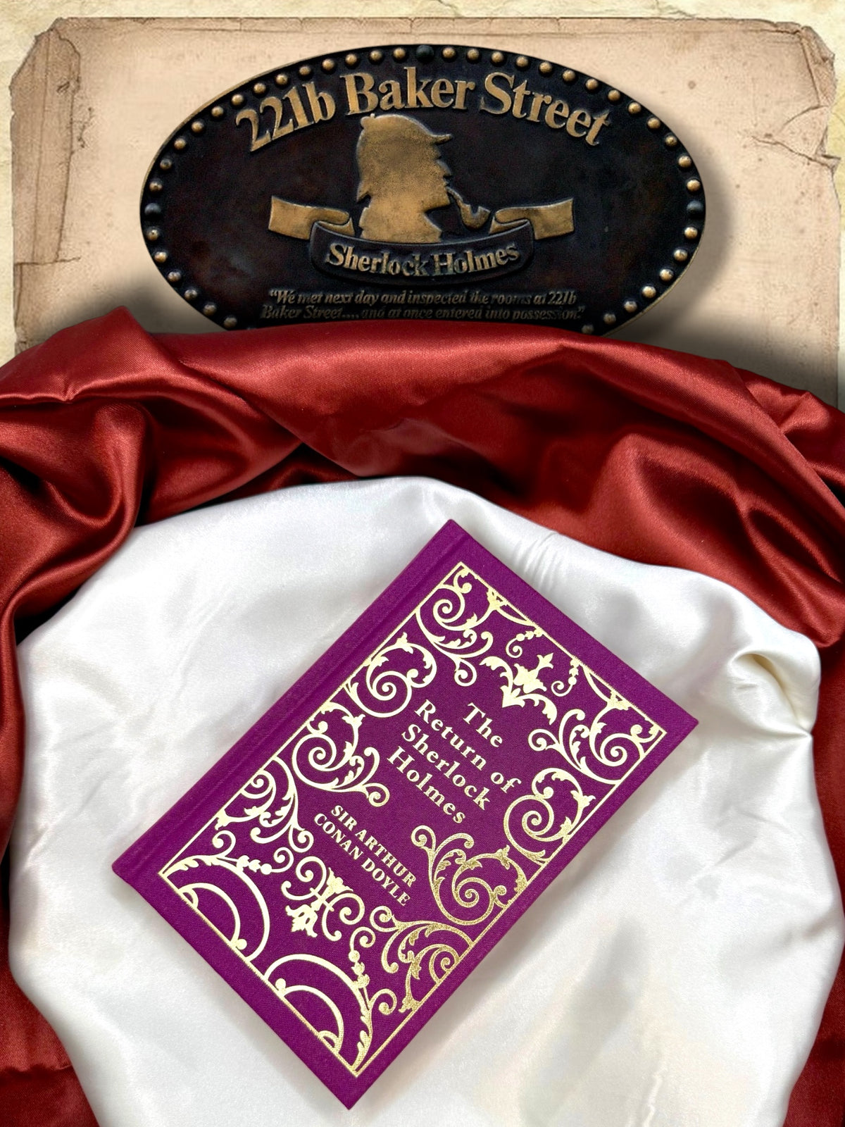 The Return of Sherlock Holmes purple and gold clothbound hardcover photographed flat on ivory satin with red fabric and a 221B Baker Street Sherlock Holmes sign.