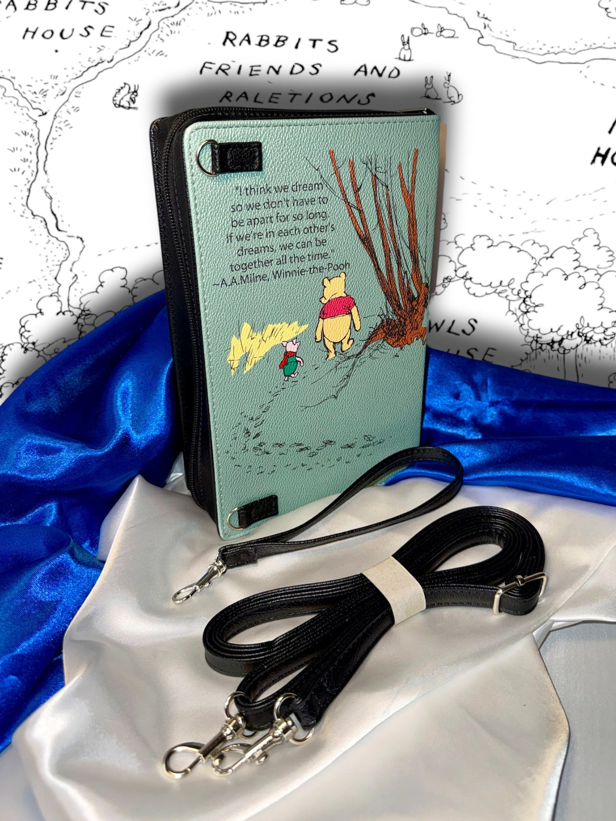 Close-up of The House at Pooh Corner book clutch showing the detachable carrying strap, zipper hardware, and book-shaped vinyl construction.
