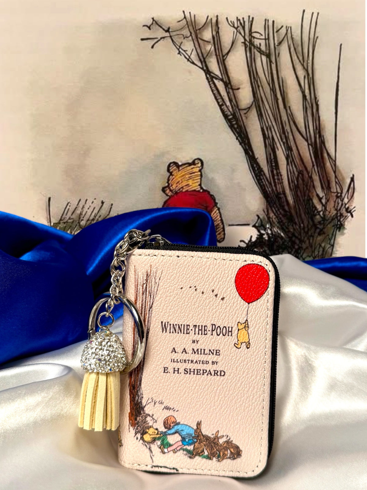 Winnie-the-Pooh miniature book coin purse and bag charm with E. H. Shepard illustrations, red balloon, silver keyring, and cream tassel on satin.