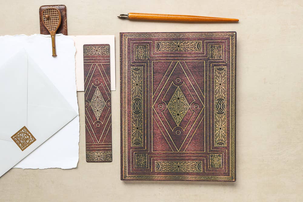 Decorative book with ornate cover on a beige surface, accompanied by a pen and envelope.