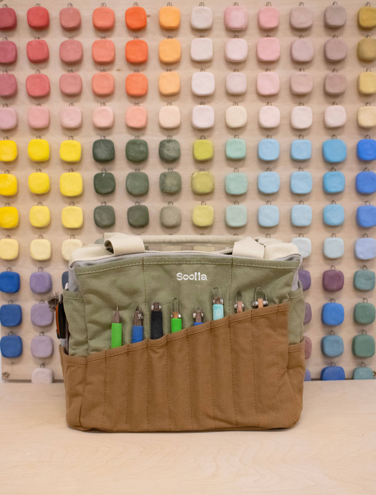 Green and brown bag with colorful items against a multicolored square patterned wall.