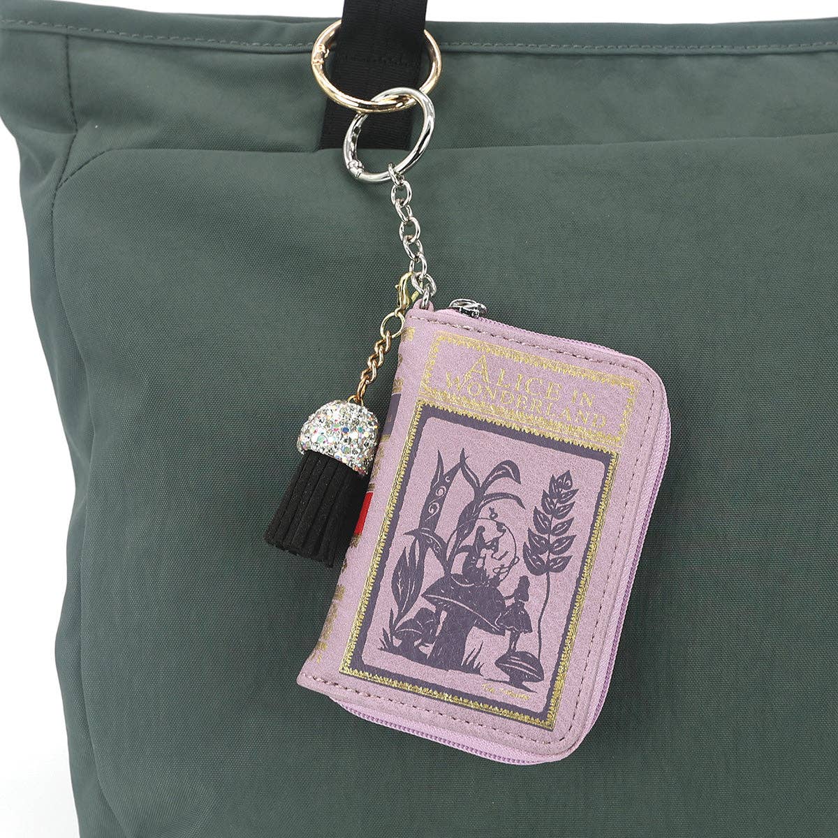 Pink book-shaped keychain with tassel on a green bag
