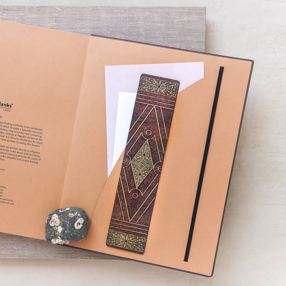 Decorative bookmark on an open notebook with a stone on a light surface