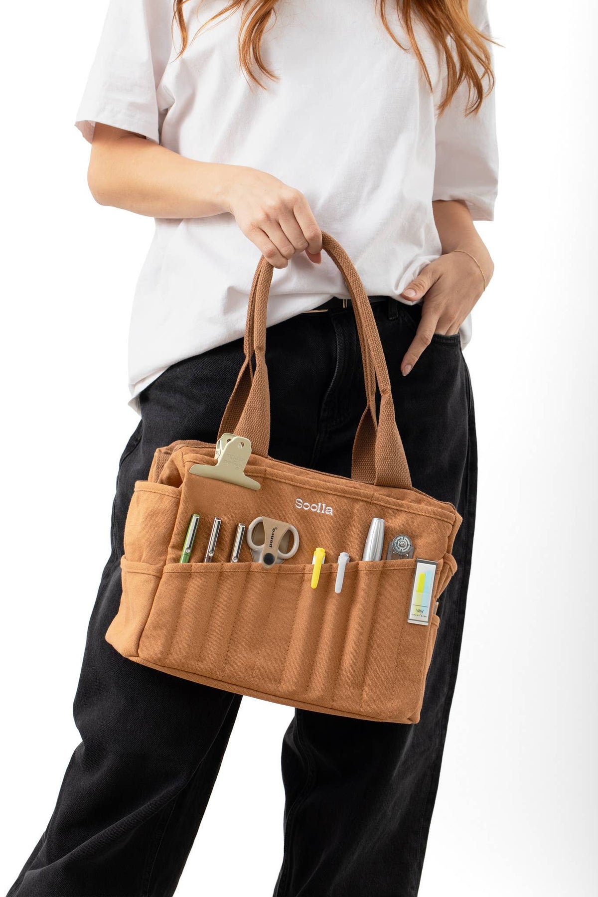 Person holding a Cinnamon Soolla Studio Artist  tool bag with various tools on a white background