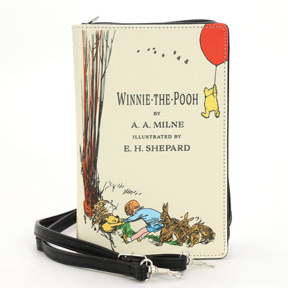 The House at Pooh Corner book clutch crossbody purse in beige, with classic Winnie-the-Pooh illustrated cover artwork and detachable carrying straps.