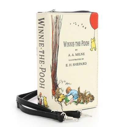 The House at Pooh Corner beige book clutch bag shown at an angle with illustrated literary cover, zipper closure, and detachable strap hardware.
