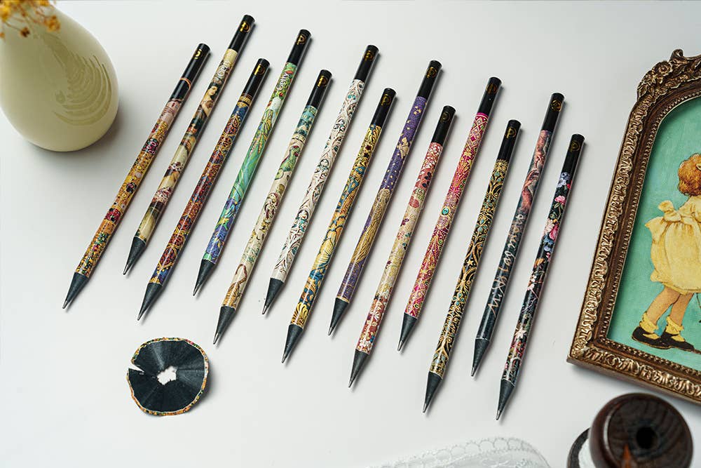 Decorative pencils with artistic designs on a white surface, framed picture in the background