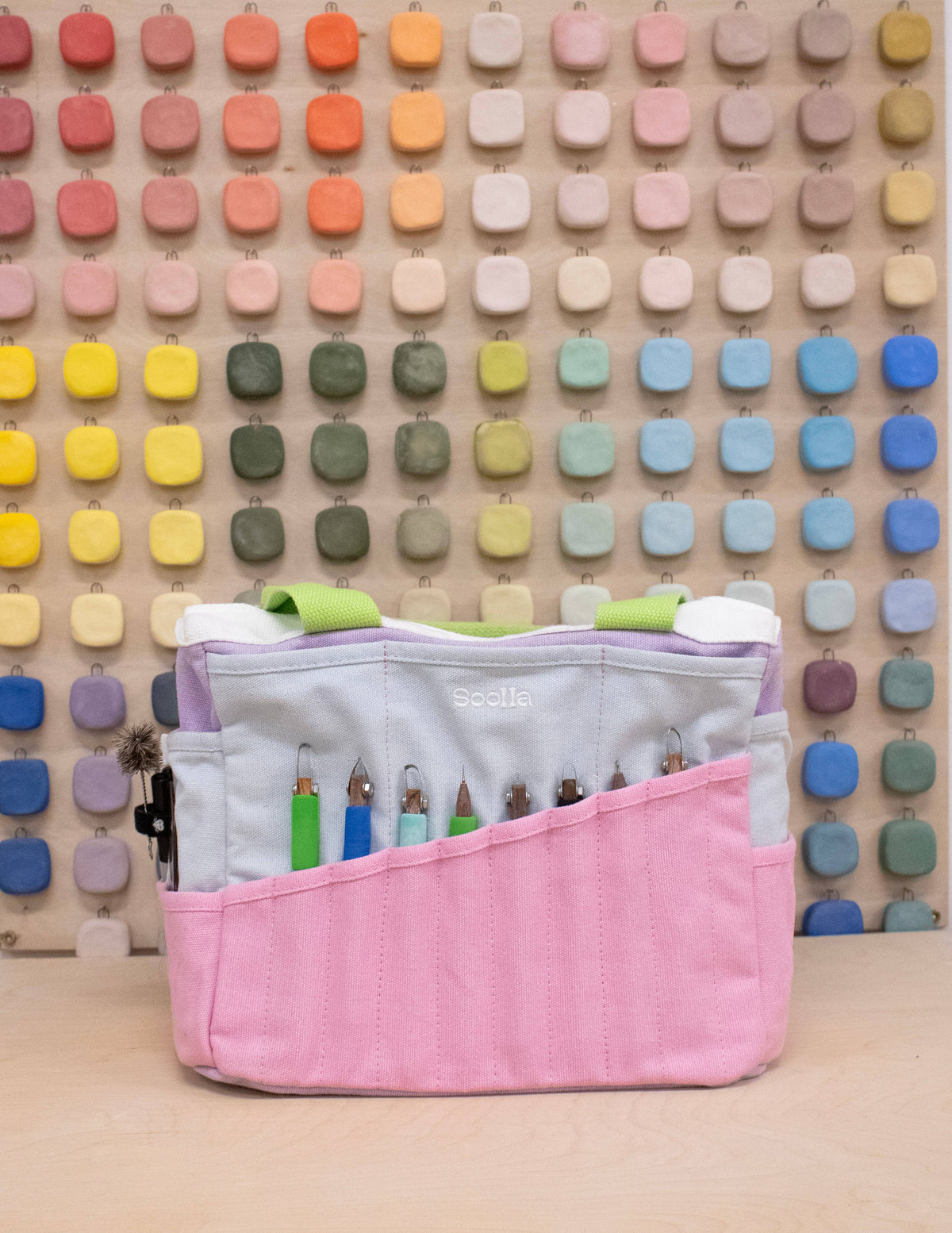 Pink craft organizer with colorful items against a patterned wall.