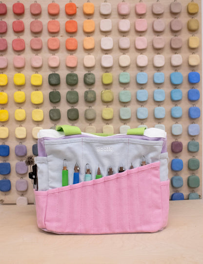 Pink craft organizer with colorful items against a patterned wall.