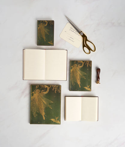 Set of green notebooks with fairy designs, scissors, and a sealing wax stamp on a white surface.