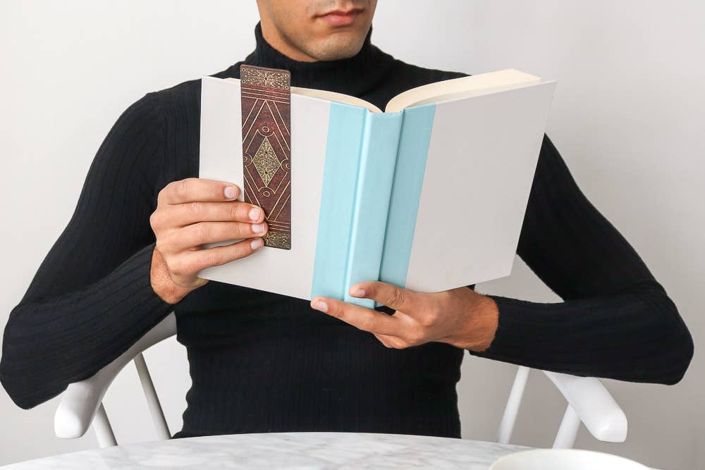 Person holding a book with a decorative bookmark against a plain background