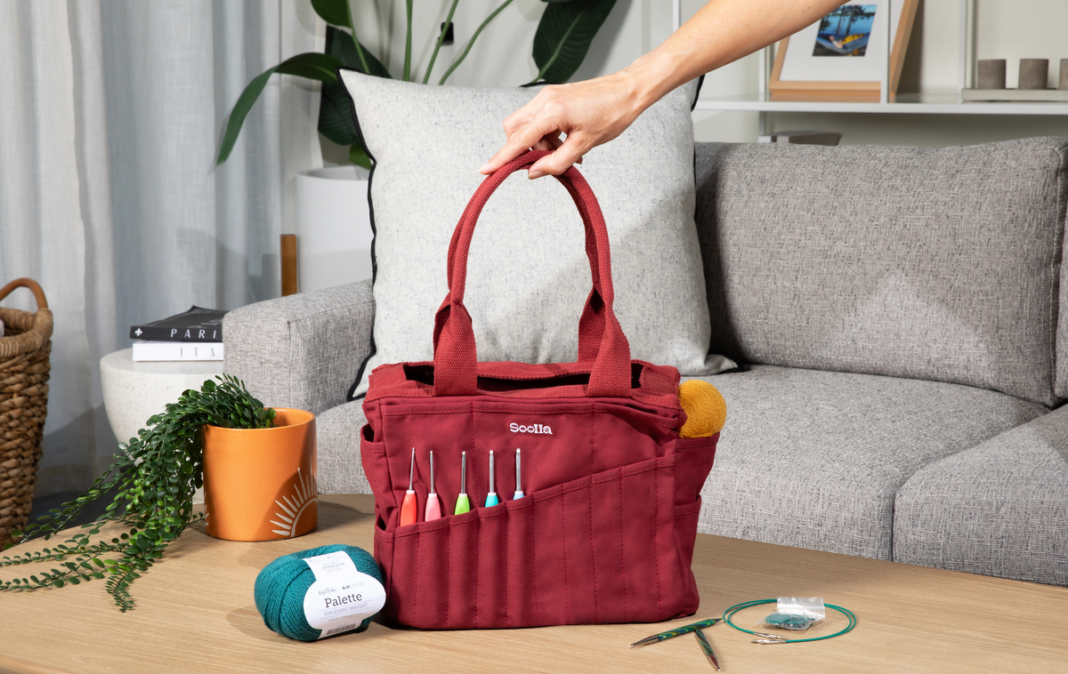 Sangria tote bag with knitting supplies on a wooden table in a living room setting