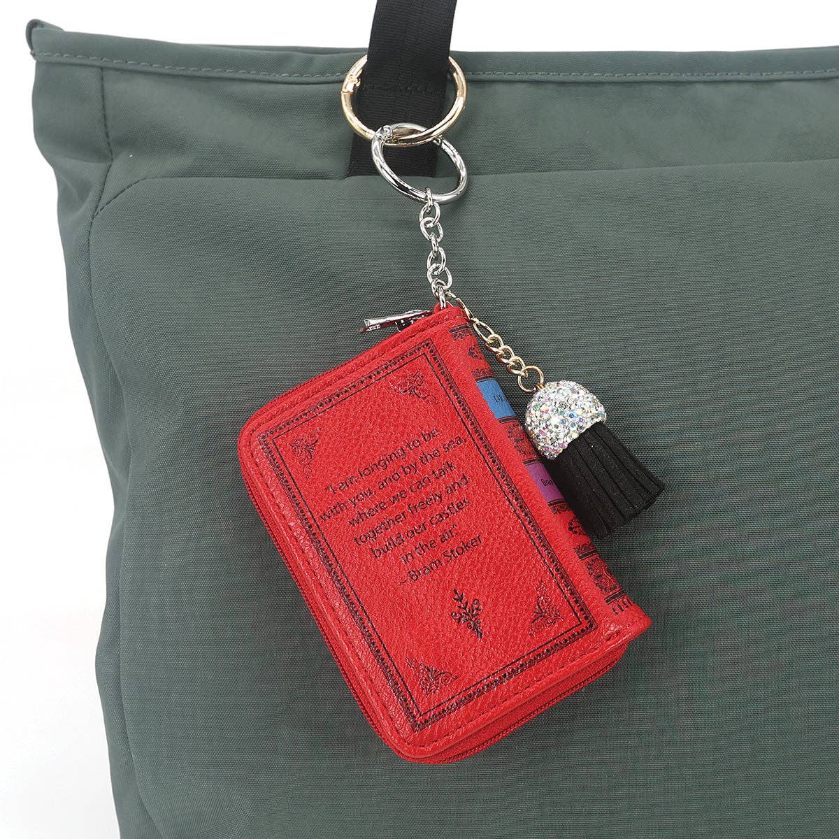 Red book-shaped keychain with tassel on a green bag