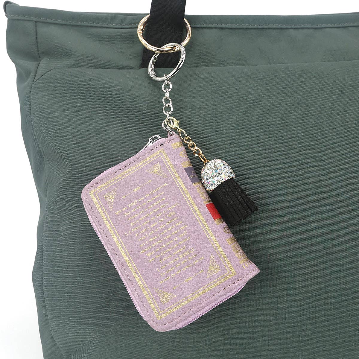 Purple book-shaped keychain with tassel hanging from a green bag
