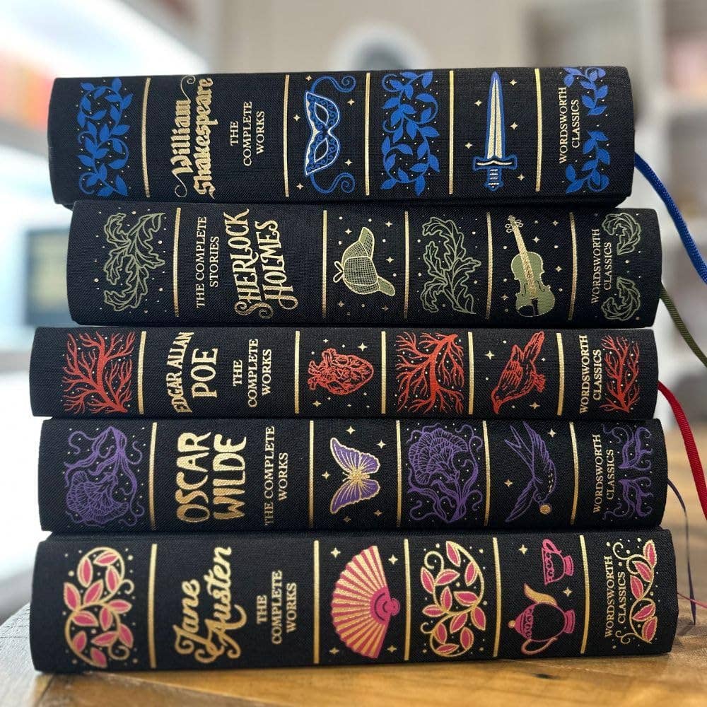 Stack of black leather-bound books with colorful embossed designs on a wooden surface.