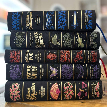 Stack of black leather-bound books with colorful embossed designs on a wooden surface.