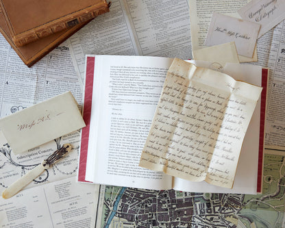 Open book with handwritten pages on a surface with old documents and a feather pen.