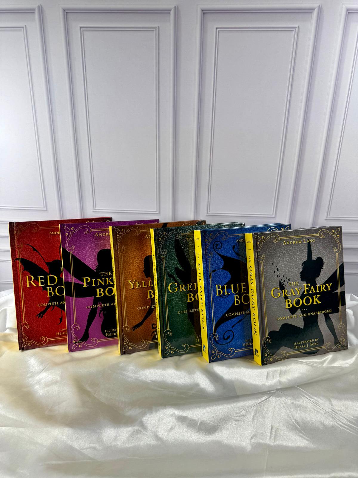 Six Andrew Lang Fairy Books displayed together: Red, Pink, Yellow, Green, Blue, and Gray, with colorful illustrated covers.