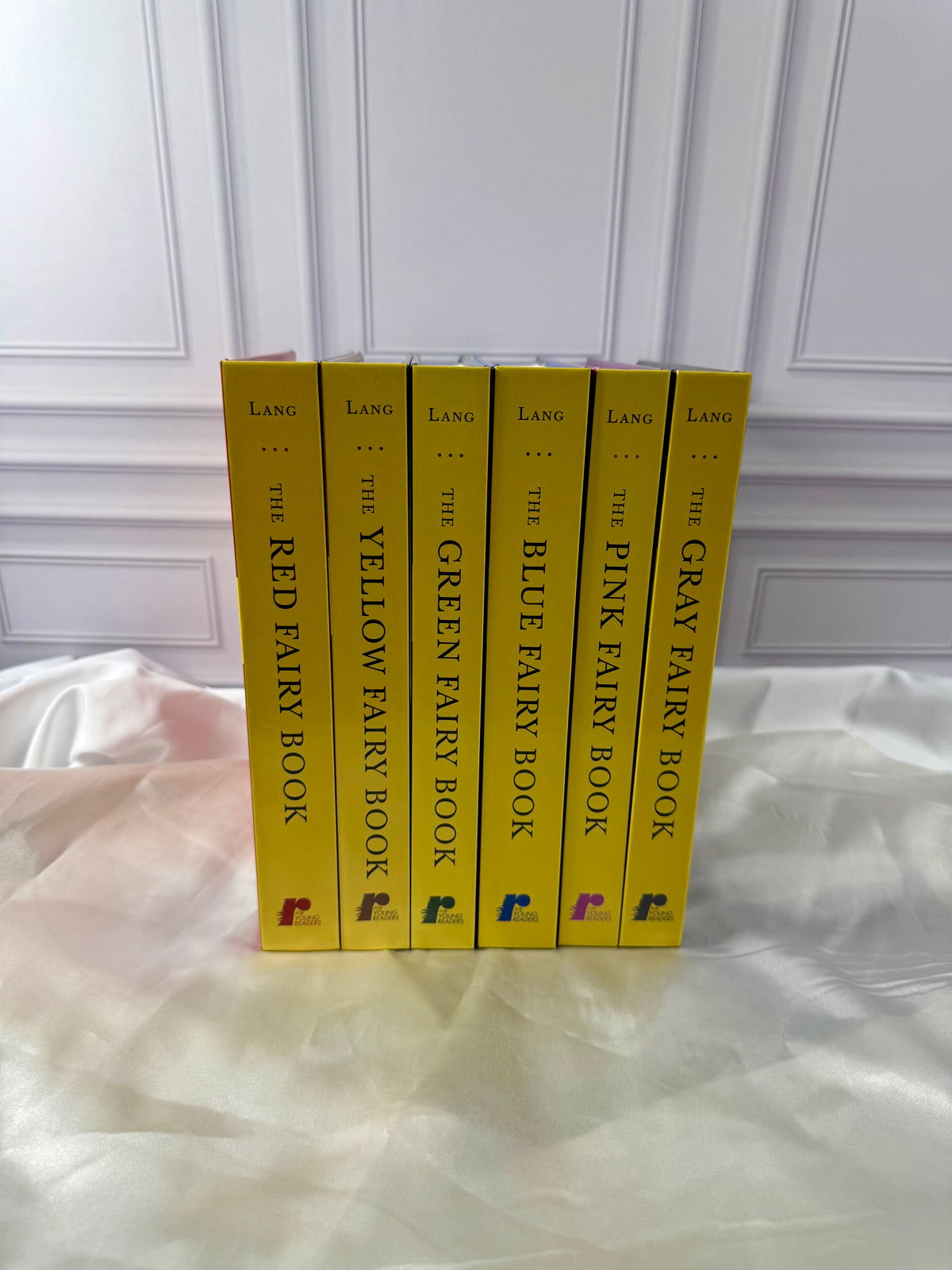 Matching yellow spines of six Andrew Lang Fairy Books: Red, Yellow, Green, Blue, Pink, and Gray, arranged side by side.