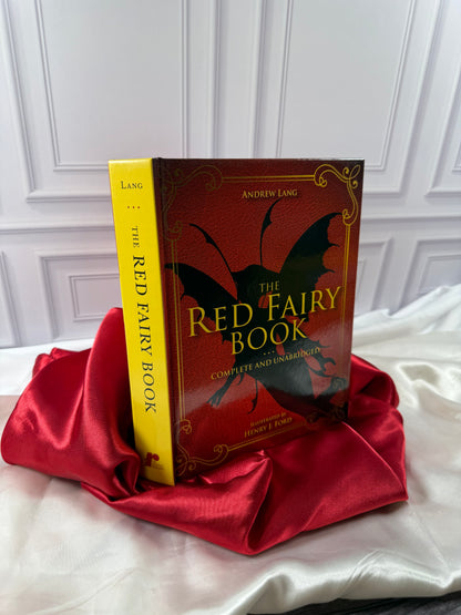 The Red Fairy Book by Andrew Lang photographed at an angle, showing its bright yellow spine and decorative red hardcover.