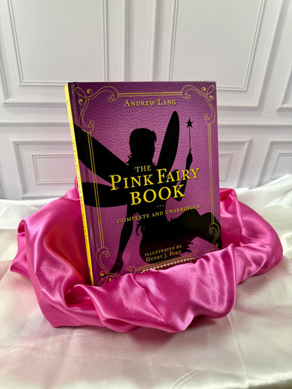 The Pink Fairy Book by Andrew Lang, illustrated hardcover with gold lettering and a fairy silhouette, styled on satin at StoryGiftStudio.