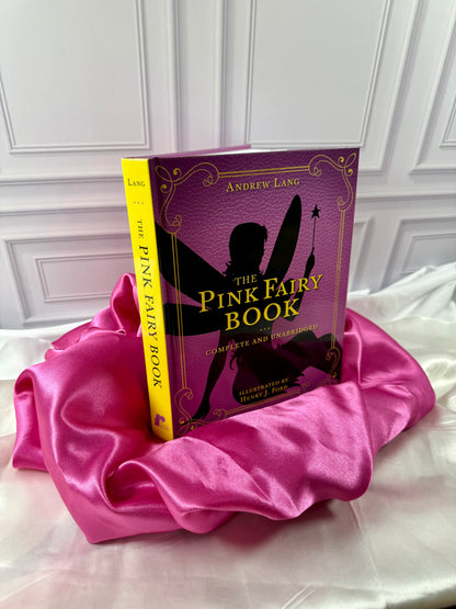 The Pink Fairy Book by Andrew Lang photographed at an angle, showing its bright yellow spine and decorative pink hardcover.
