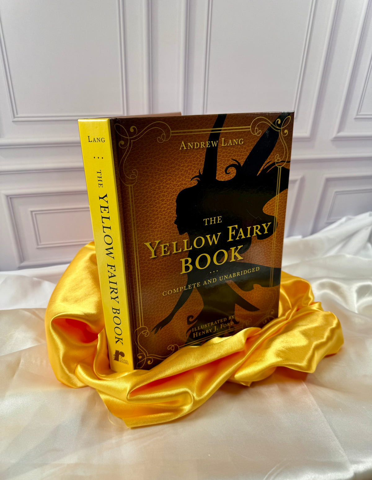 The Yellow Fairy Book by Andrew Lang photographed at an angle, showing its bright yellow spine and decorative yellow hardcover.