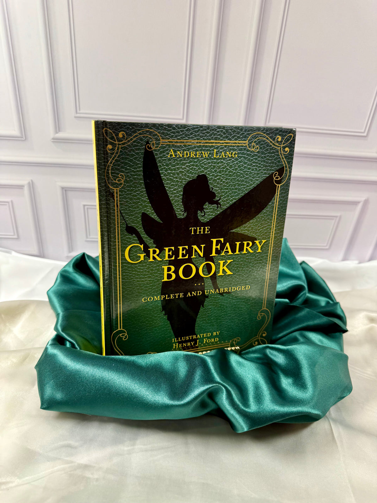 Green Fairy Book by Andrew Lang, illustrated hardcover with gold lettering and fairy silhouette, displayed on emerald satin at StoryGiftStudio.