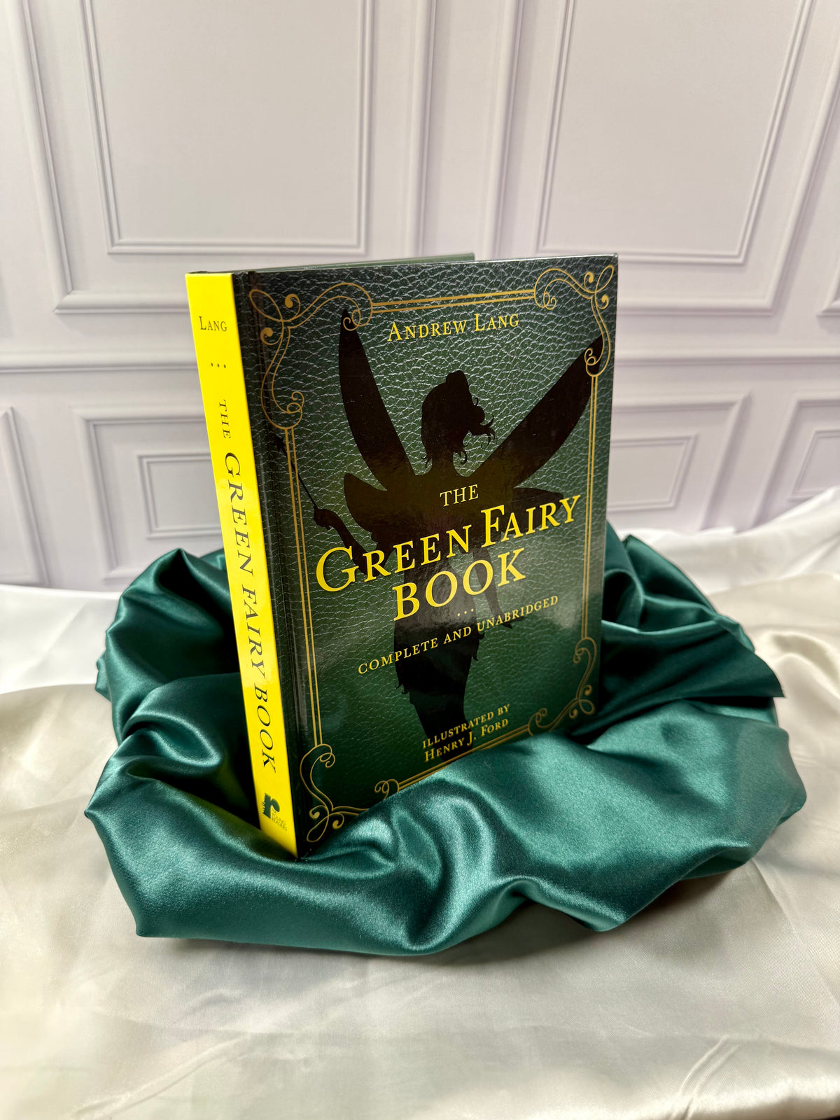 Green Fairy Book by Andrew Lang shown at an angle, displaying its bright yellow spine and decorative green hardcover on emerald satin.