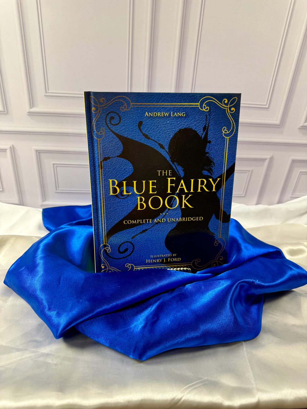 The Blue Fairy Book by Andrew Lang, illustrated blue hardcover with decorative gold lettering, displayed on satin at StoryGiftStudio.