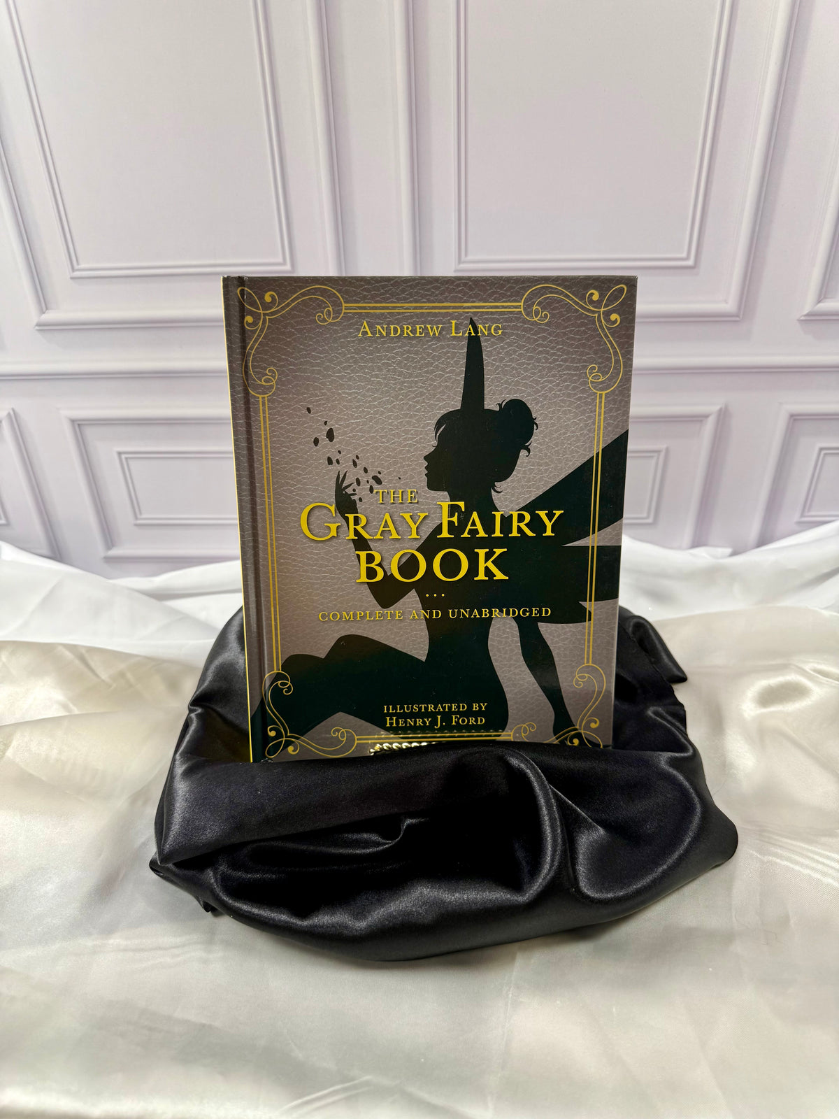The Gray Fairy Book by Andrew Lang, illustrated hardcover with gold lettering and fairy silhouette, styled on satin at StoryGiftStudio.