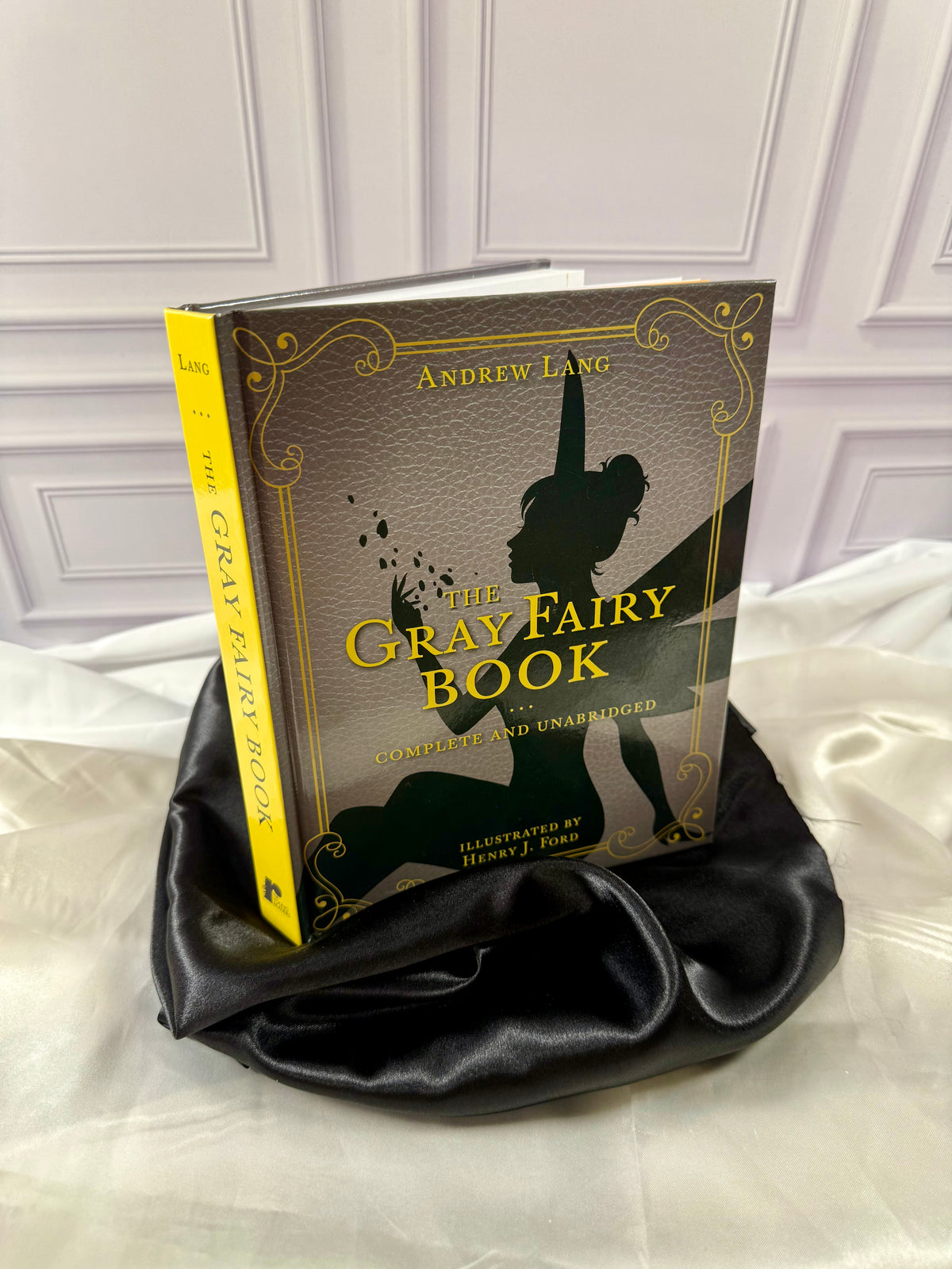 The Gray Fairy Book by Andrew Lang photographed at an angle, showing its bright yellow spine and decorative gray hardcover.