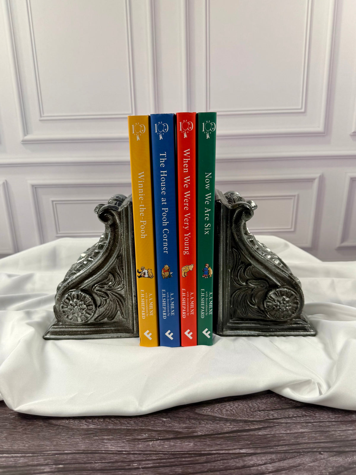Four matching A. A. Milne 100th anniversary hardcover books displayed with colorful spines together: Winnie-the-Pooh, The House at Pooh Corner, When We Were Very Young, and Now We Are Six.