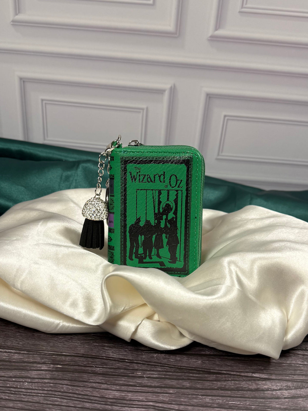 The Wizard of Oz miniature book bag charm and coin purse with emerald green cover, black storybook illustration, silver keyring, and decorative black tassel.