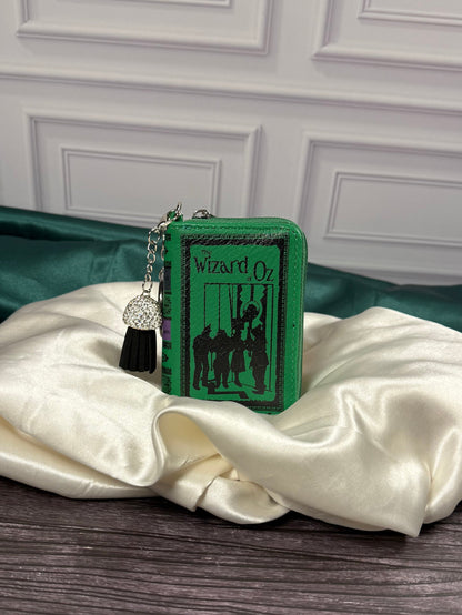The Wizard of Oz miniature book bag charm and coin purse with emerald green cover, black storybook illustration, silver keyring, and decorative black tassel.