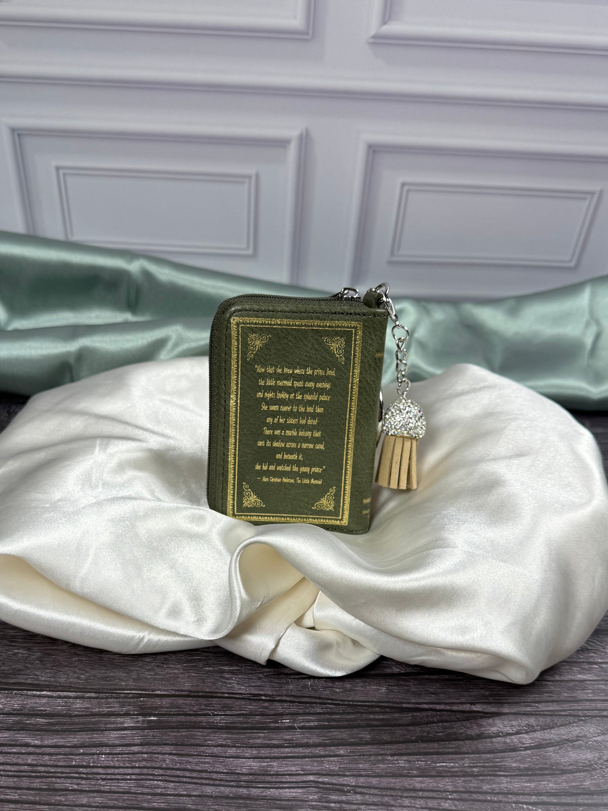 Back cover of The Little Mermaid book bag charm featuring gold decorative text and border on olive green vinyl, with silver keyring and tassel.